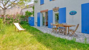 A building with blue shutters, a patio with a table and chairs, and a garden with flowers. - Holiday Home 'Maison Albizia' with Private Terrace, Garden, and Wi-Fi (Le Croisic)