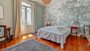 A bedroom with a bed, wooden floor, a window with curtains, a wall with a tree mural, and a hanging light fixture. - Holiday Home 'Maison Albizia' with Private Terrace, Garden, and Wi-Fi (Le Croisic)