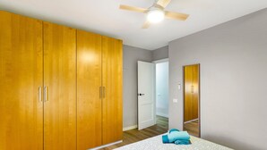 Un dormitorio con un armario grande, un ventilador de techo y una cama con colcha estampada.