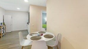 Una cocina moderna con electrodomésticos blancos, una mesa de comedor con cuatro sillas y vistas a un espacio exterior verde.