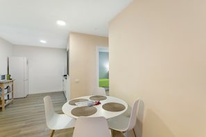A modern kitchen with white appliances, a dining table with four chairs, and a view of a green outdoor area. - Vacation Apartment 'Apartamento Con Piscina Arinaga' with Shared Pool and Wi-Fi (Arinaga)