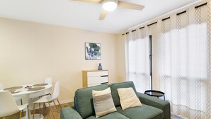 Un salón con un sofá verde, sillas blancas, una mesita y un ventilador de techo.
