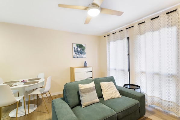 A living room with a green sofa, white chairs, a small table, and a ceiling fan.
