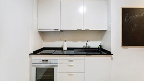Una cocina compacta con armarios blancos, encimera negra, horno integrado y una pizarra con la palabra 'Bienvenidos'.