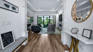 Ein modernes Interieur mit Holzboden, einer schwarzen Couch, einem grauen Sessel, einem Marmorkonsolentisch und einem großen Spiegel mit goldener Rahmung.