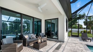 Ein moderner Außenbereich mit Korbmöbeln, Deckenventilator und Blick auf einen Swimmingpool.