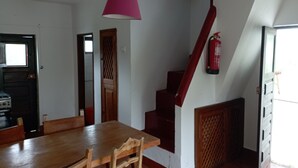 Ein Essbereich mit Holztisch und Stühlen, einer rosa Pendelleuchte, einer Treppe mit roter Handlauf und einem an der Wand befestigten Feuerlöscher.