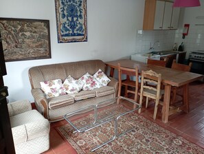 A living room with a sofa, a dining table, chairs, a rug, and a kitchen in the background. - Country House 'Refúgio Da Montanha' with Mountain View, Private Terrace and Private Garden (Sobral)
