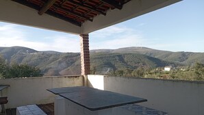 Ein Balkon mit Tisch und Bänken, mit Blick auf eine gebirgige Landschaft mit Windkraftanlagen.
