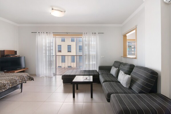 Un salon moderne avec un canapé, un téléviseur et un balcon agrémenté de rideaux.