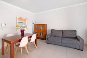 Un coin repas avec une table et des chaises en bois, un canapé gris, un meuble et un thermostat fixé au mur.