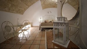 A bedroom with a stone ceiling, a bed, a bedside table, a chair, and a mirror.