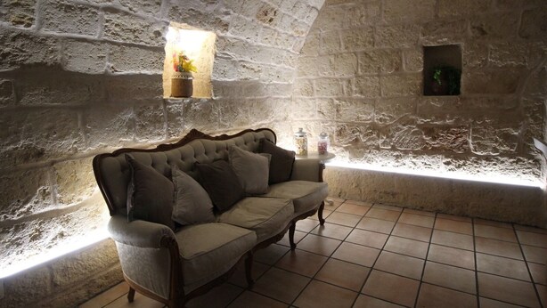 A stone-walled room with a cushioned bench, a small window with a plant, and a tiled floor.