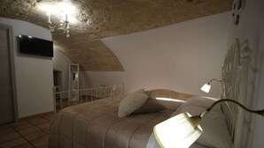 A bedroom with a bed, a bedside lamp, a TV, and a stone ceiling.