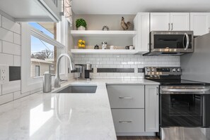 A modern kitchen with white cabinetry, a stainless steel stove, a microwave, and a sink. - 1216 Lambeau Field Luxe (Green Bay)