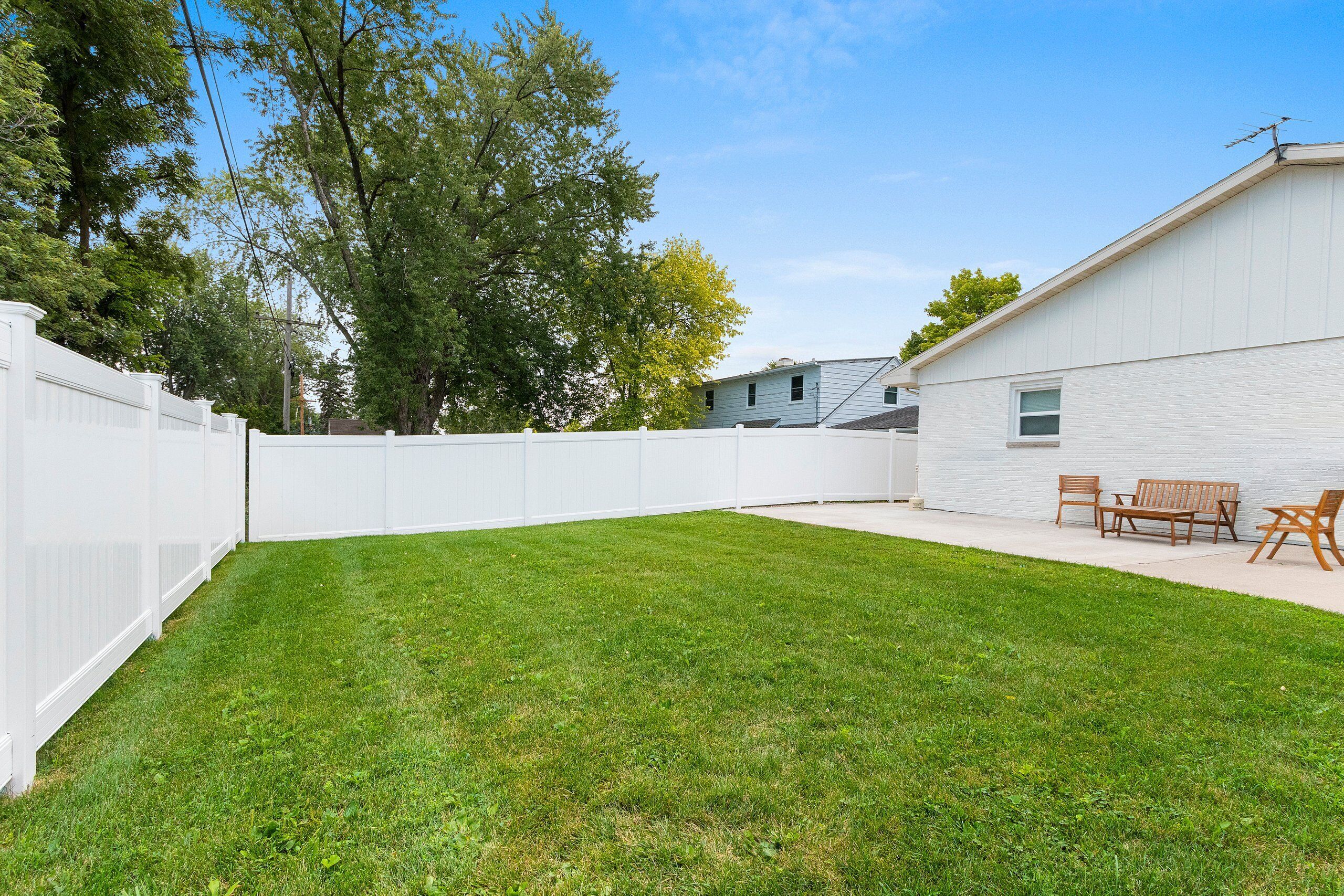 A backyard with a white fence, a grassy lawn, and a building with a window and a door.