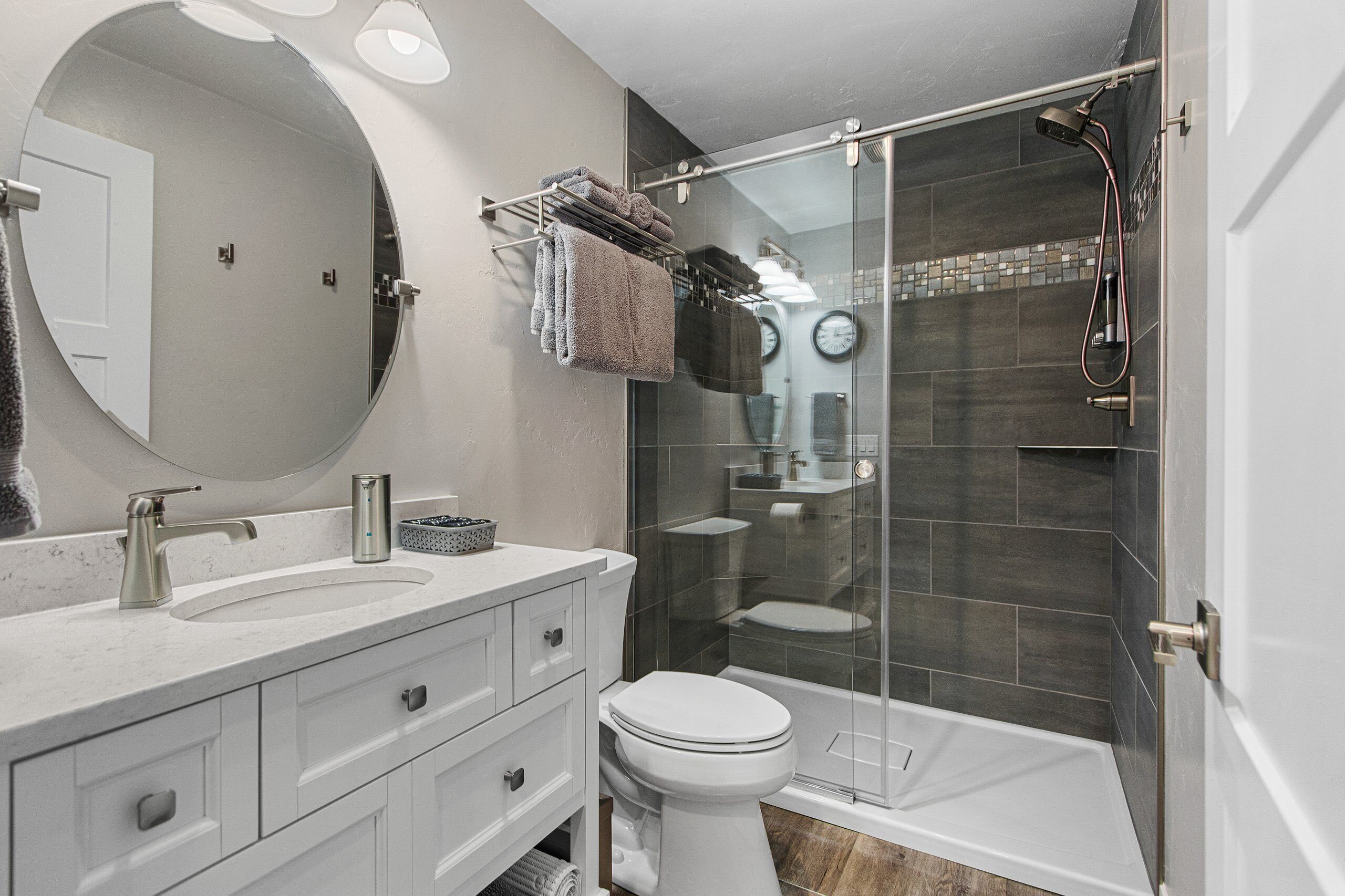 Une salle de bain moderne avec un meuble-lavabo blanc, un miroir rond, une cabine de douche en verre et des toilettes.