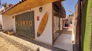 A building with a sign reading 'PUERTO,' a wooden surfboard, and a tiled pathway leading to a door. - Hotel Boutique Puerto (Máncora)