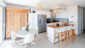 Een moderne keuken met witte kasten, een roestvrijstalen koelkast en een houten kookeiland met barstoelen.