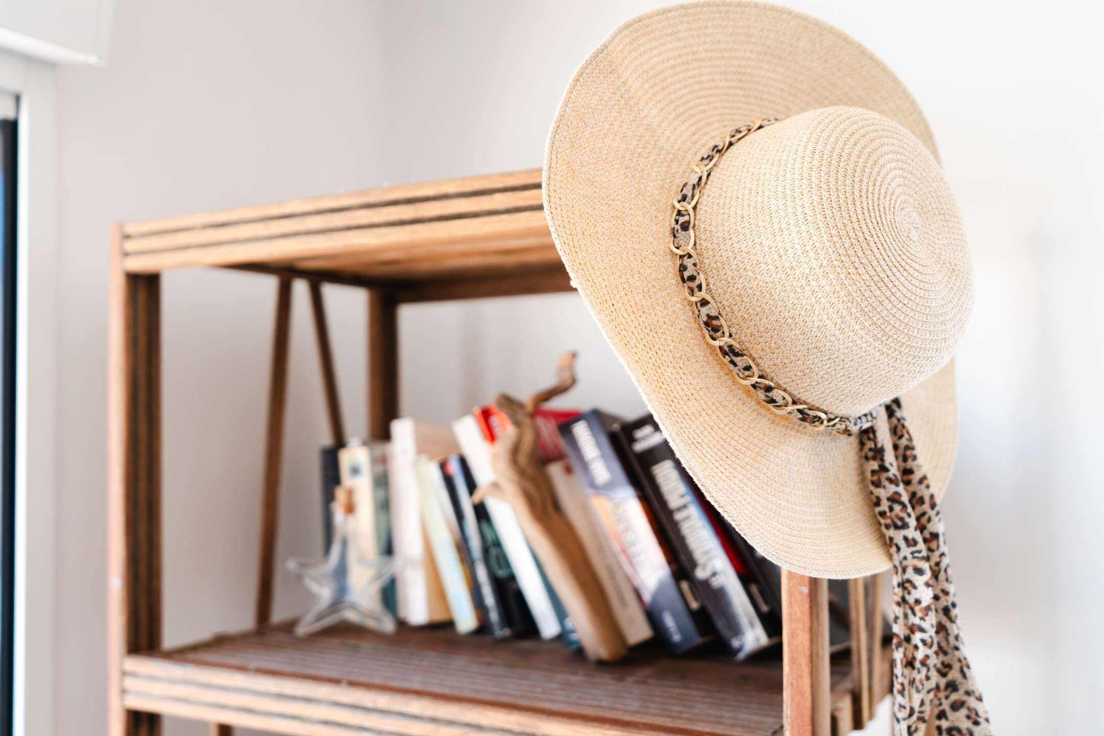 A straw hat with a leopard print band on a wooden shelf.