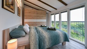Un dormitorio con una cama grande, cabecero de madera y un balcón con vistas a zonas verdes.