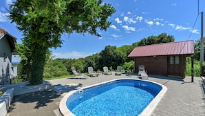 Una piscina con sillas de descanso, una cabaña de madera y un árbol.