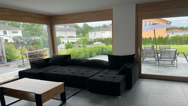 Ein modernes Wohnzimmer mit einem Ecksofa, einem Holztisch und einer Schiebetür zu einer Außenpatio mit Tisch und Stühlen.