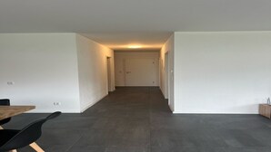 Ein schmaler Flur mit dunklen Fliesen, weißen Wänden und einer Tür am Ende.