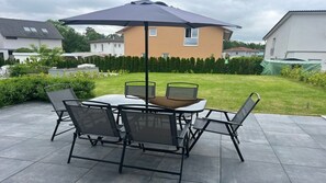 An outdoor patio with a round table and four chairs, a large umbrella, and a well-maintained lawn.