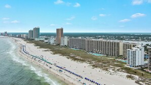 Eine Küstenstadtansicht mit Hotelbereich direkt am Strand, einschließlich hoher Gebäude, einem Sandstrand und blauem, wolkenlosem Himmel.