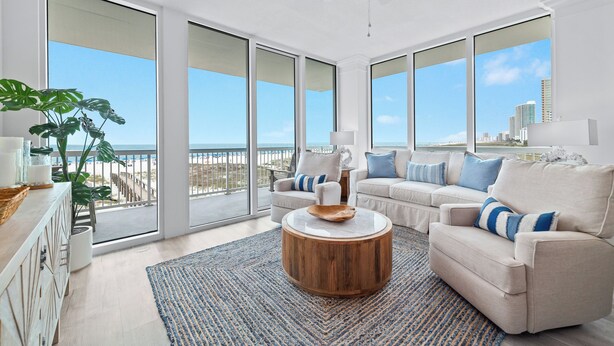 Ein geräumiges Wohnzimmer mit großen Fenstern, einem Deckenventilator und Blick auf den Strand.