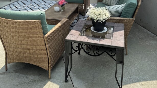 Eine Terrasse mit Korbmöbeln, einem Tisch mit Blumenvase und einem großen Sonnenschirm.