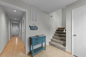 Un couloir doté d’un plancher en bois, d’une console bleue avec des tiroirs, d’une enseigne fixée au mur et d’un escalier recouvert de moquette.