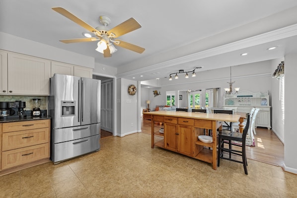 A spacious kitchen with a central island, stainless steel appliances, wooden cabinets, and a ceiling fan.