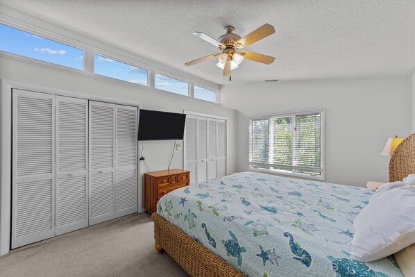 Une chambre à coucher comprenant un lit, un ventilateur de plafond, une armoire, une fenêtre avec des stores et un téléviseur fixé au mur.