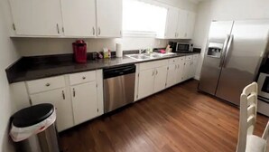Una cocina con gabinetes blancos, lavavajillas de acero inoxidable, microondas y refrigerador.