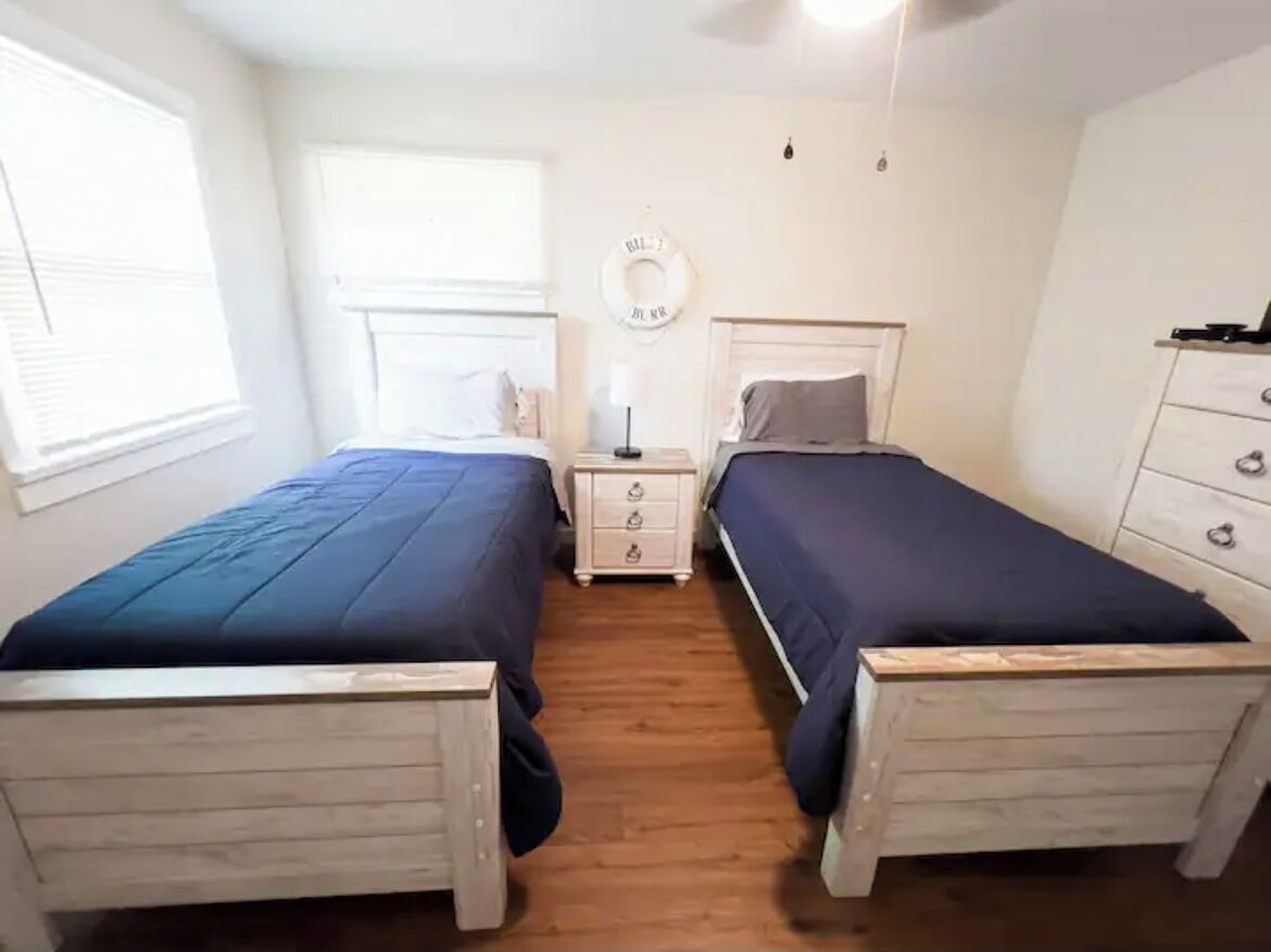 Un dormitorio con dos camas individuales, una mesita de noche con lámpara, un aparador y un adorno circular en la pared.