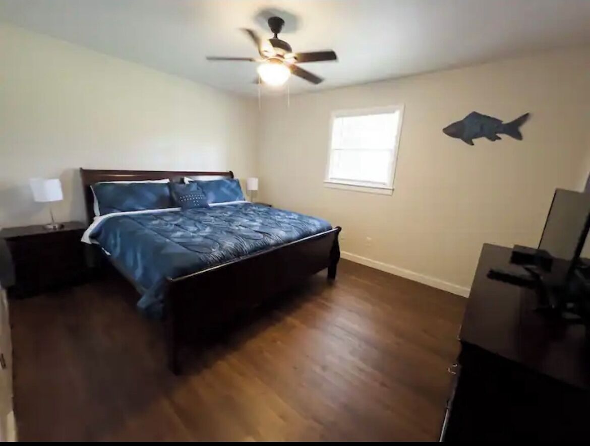 Un dormitorio con una cama, un ventilador de techo, una ventana y un adhesivo con forma de pez en la pared.