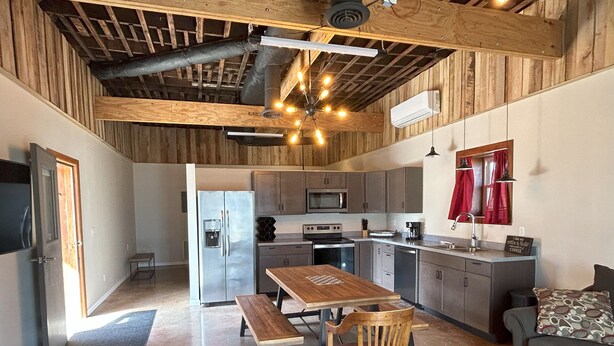 Una cocina moderna con techo de madera, electrodomésticos de acero inoxidable y un comedor con mesa y sillas de madera.