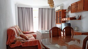 Una sala de estar acogedora con sofá, mesa de comedor y zona de cocina con armarios de madera y televisor.