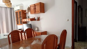 Un comedor con una mesa de vidrio y sillas de madera, un armario de madera con puertas de cristal, y un televisor sobre una mesita.
