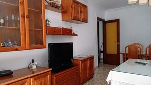 Una habitación con un armario de madera, un televisor, una mesa con mantel blanco y una puerta al fondo.