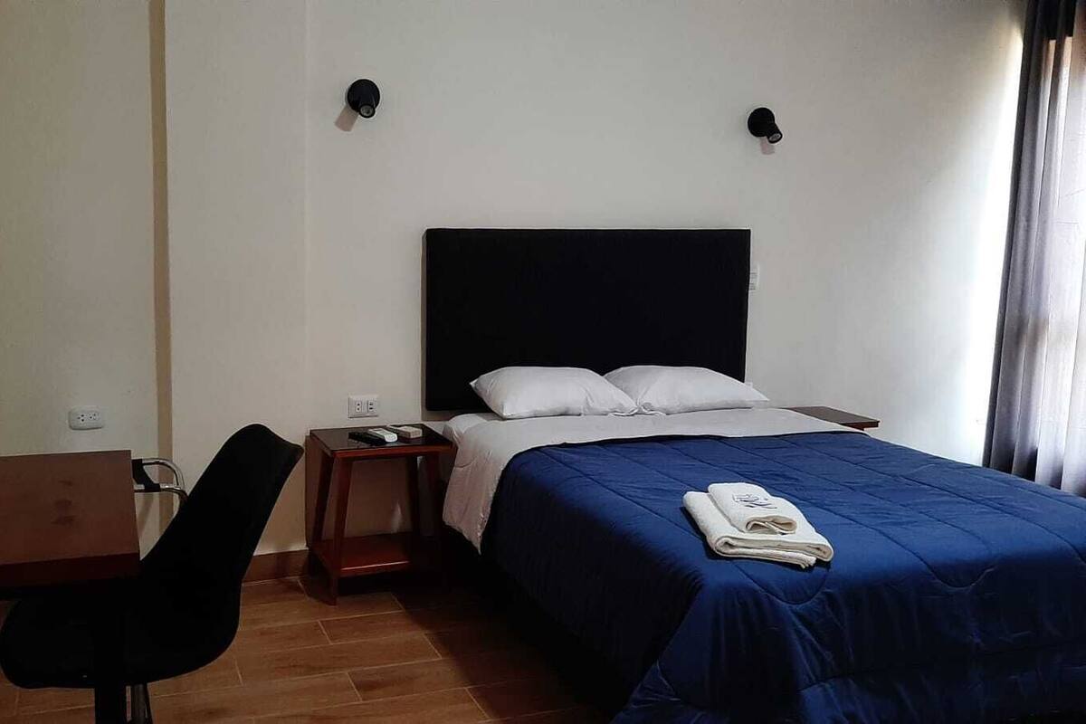 A hotel room with a single bed, a desk, a chair, and a nightstand.