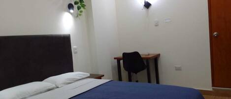 A bedroom with a bed, a desk, a chair, and a door.