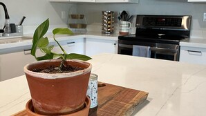 A kitchen with white cabinets, a microwave, and an oven. There is a potted plant on a wooden board.