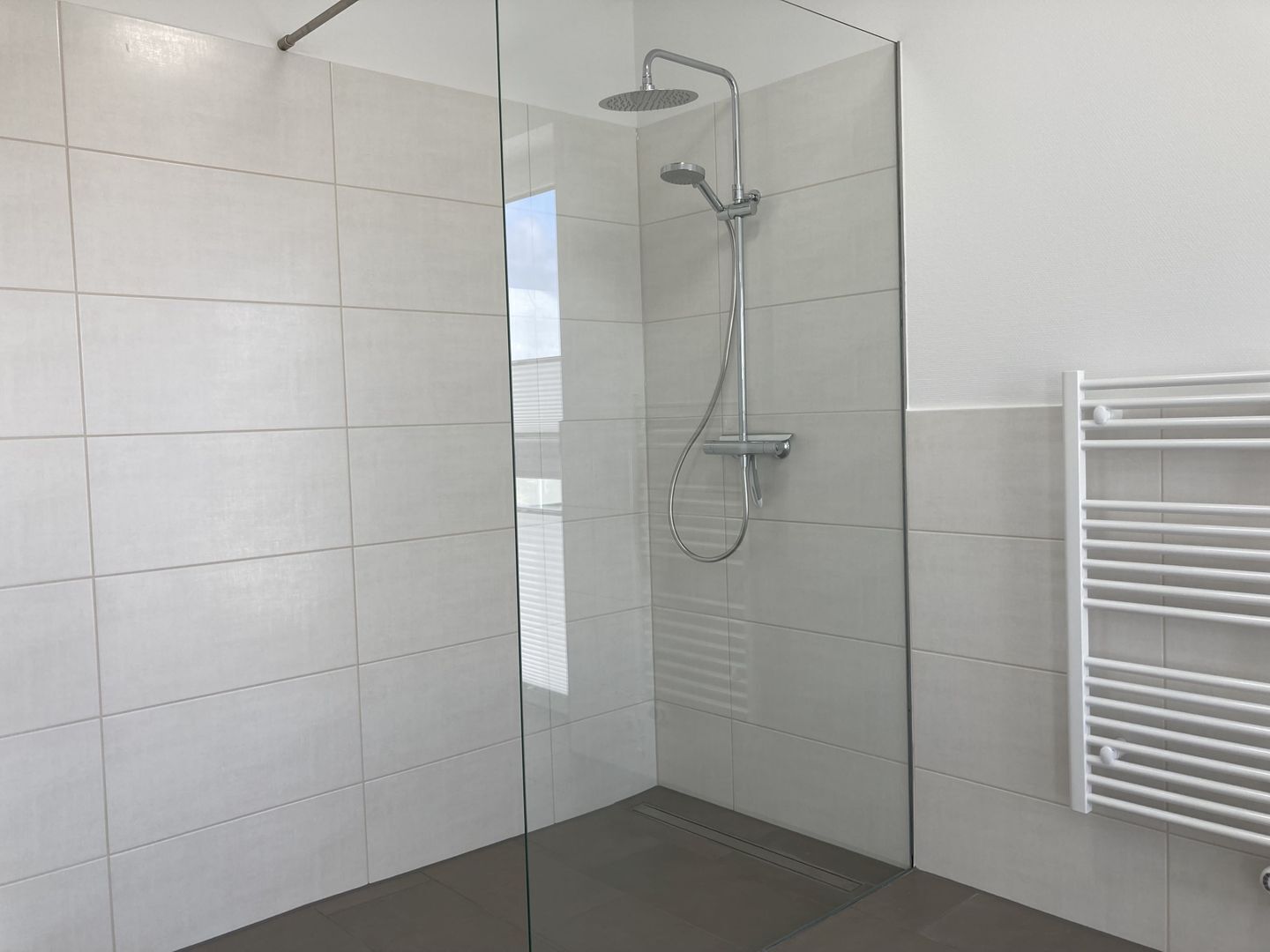 A modern bathroom with a glass shower enclosure, white tiled walls, and a white towel rack.
