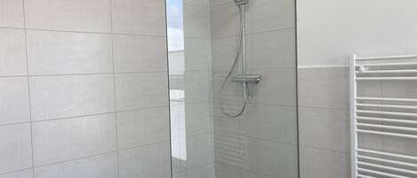 A modern bathroom with a glass shower enclosure, white tiled walls, and a white towel rack.