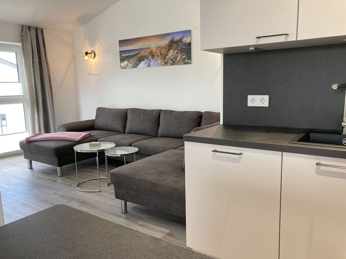 A modern living room with a sectional sofa, a small round table, and a kitchen area with a countertop and cabinets.