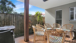 A patio with a wooden deck, wicker chairs, a table, and a wooden fence. - Bennett’s Beach Townhouse (Hawks Nest)