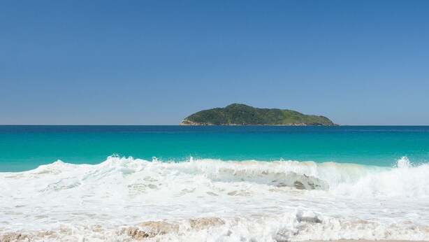 A beach with waves crashing onto the shore and a small island in the distance. - Bennett’s Beach Townhouse (Hawks Nest)